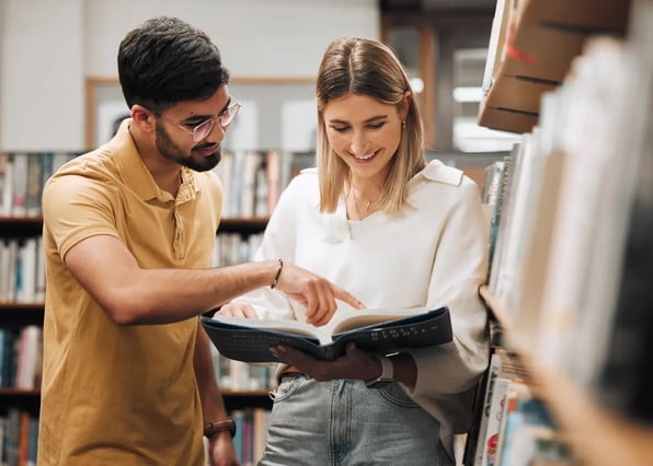 Dos estudiantes de Derecho consultan un libro en la biblioteca de la universidad