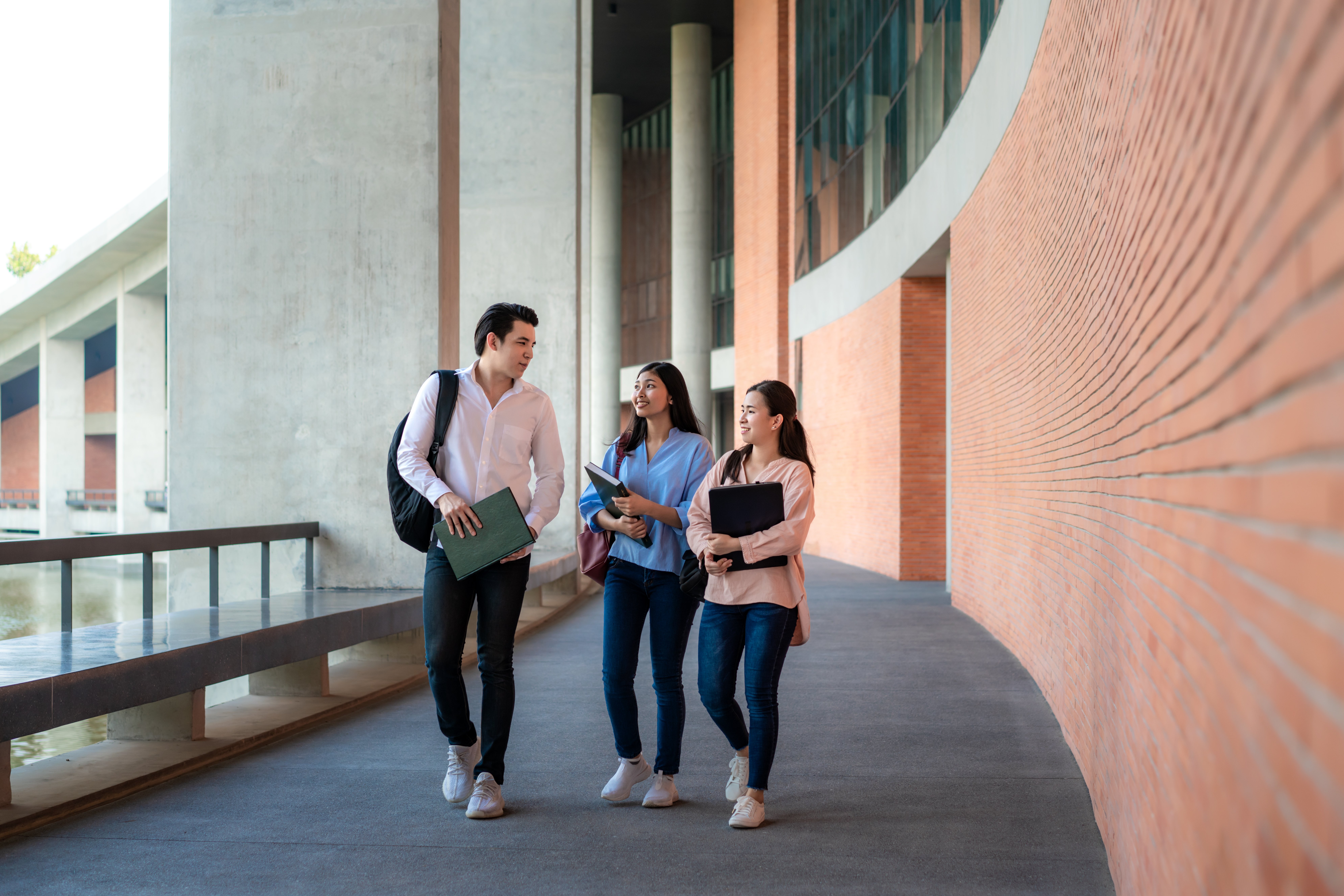 tres-estudiantes-asiaticos-estan-caminando-y-hablando-juntos-en-la-sala-de-la-universidad-durante-las-vacaciones-en-la-universidad